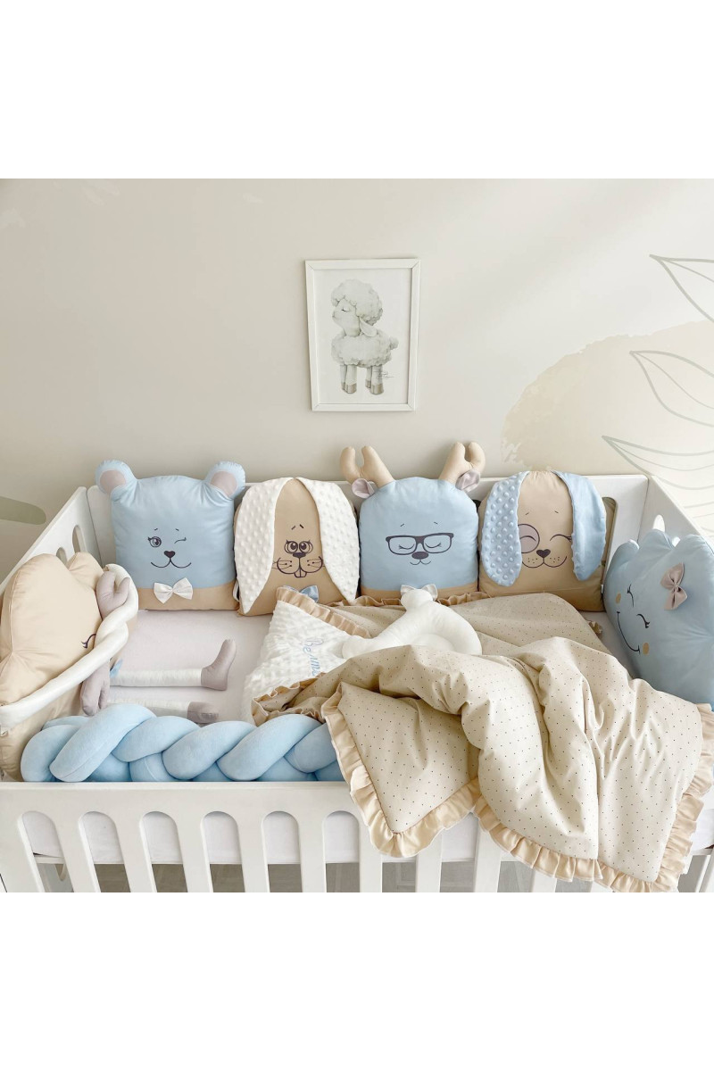 Ensemble de linge de lit pour bébé avec des coussins en forme d’animaux, dans des tons pastel bleu ciel et beige.